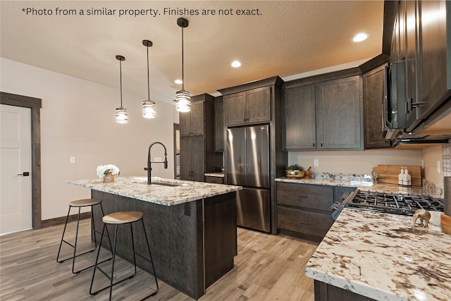 kitchen featuring light hardwood / wood-style floors, a kitchen island with sink, sink, stainless steel refrigerator, and decorative light fixtures