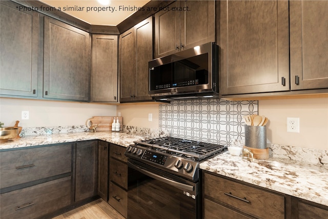 kitchen featuring light stone countertops, light wood-type flooring, black gas range oven, and dark brown cabinetry