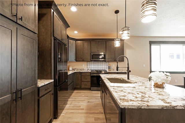 kitchen featuring light wood-type flooring, sink, a center island with sink, appliances with stainless steel finishes, and decorative light fixtures