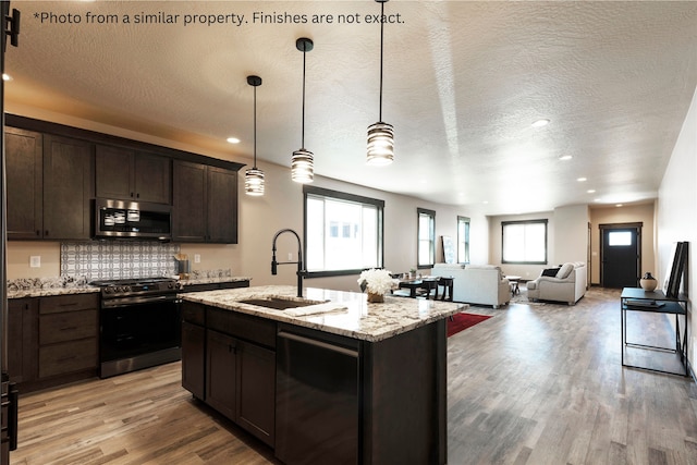 kitchen featuring a kitchen island with sink, stainless steel appliances, a textured ceiling, and a healthy amount of sunlight