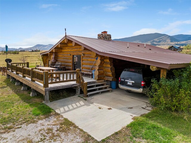 exterior space with a chimney, log exterior, driveway, a carport, and metal roof