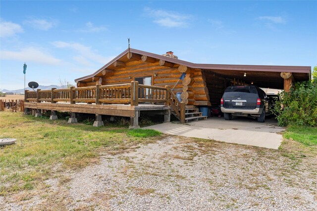 exterior space with driveway, a chimney, an attached carport, and log exterior