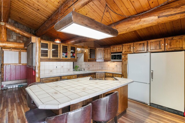 kitchen with stainless steel microwave, freestanding refrigerator, tile countertops, and wooden ceiling