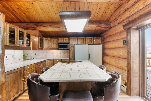 kitchen with tile counters, rustic walls, brown cabinets, stainless steel microwave, and wood ceiling
