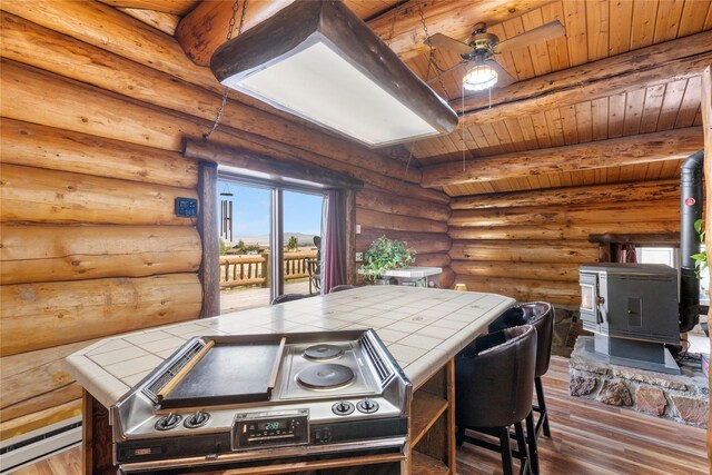 kitchen featuring beam ceiling, hardwood / wood-style floors, wooden ceiling, tile countertops, and a wood stove