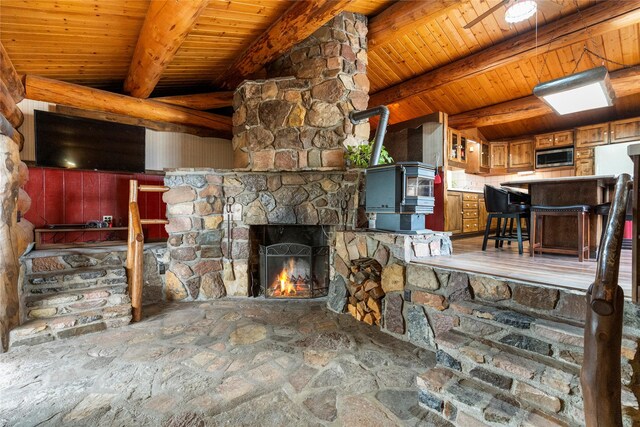 living area featuring stone flooring, a stone fireplace, beam ceiling, and wooden ceiling