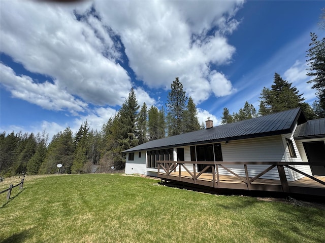 rear view of property with a wooden deck, a chimney, a yard, and metal roof