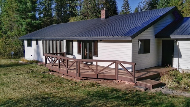 rear view of house with a chimney, a wooden deck, a yard, and metal roof
