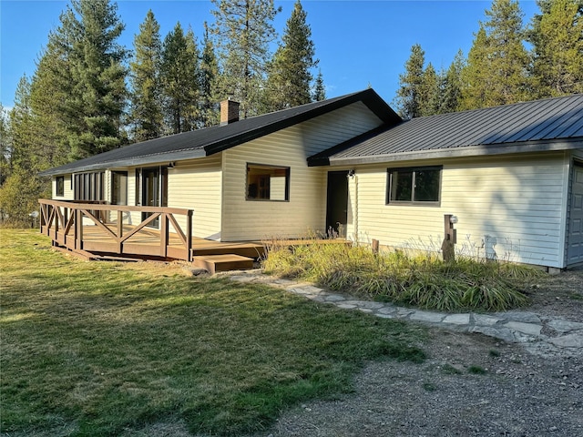 back of property featuring a lawn, a chimney, metal roof, an attached garage, and a wooden deck