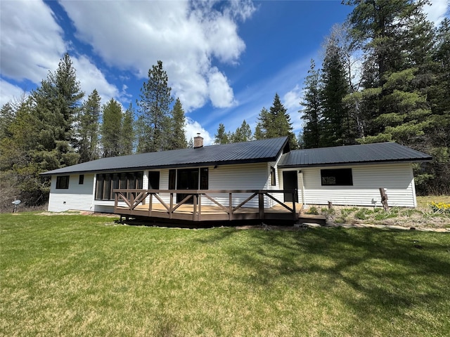 rear view of property with a chimney, a deck, metal roof, and a lawn