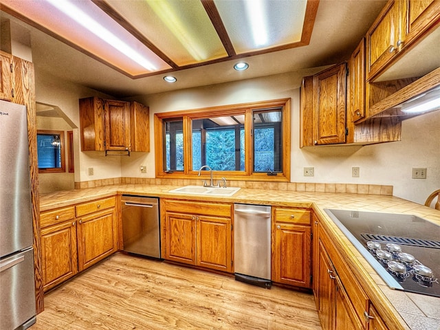 kitchen featuring tile countertops, light wood-style flooring, stainless steel appliances, a sink, and brown cabinets