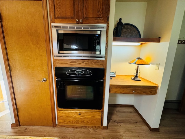 kitchen featuring wood finished floors, black oven, light countertops, brown cabinetry, and stainless steel microwave