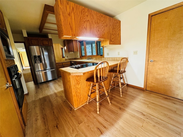 kitchen featuring brown cabinets, black oven, stainless steel fridge, a peninsula, and a kitchen breakfast bar