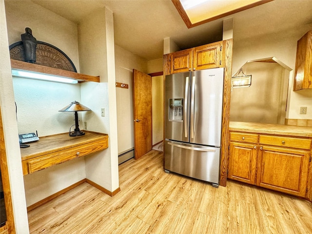 kitchen with a baseboard radiator, brown cabinets, light countertops, stainless steel fridge, and light wood-style flooring