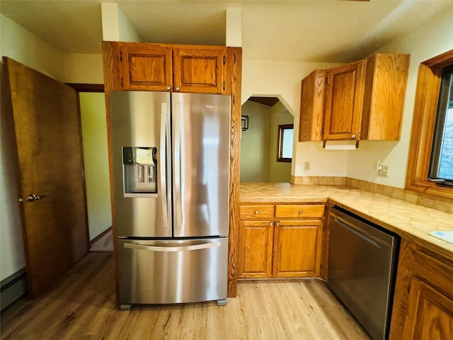 kitchen with brown cabinets, light wood finished floors, a baseboard radiator, and appliances with stainless steel finishes