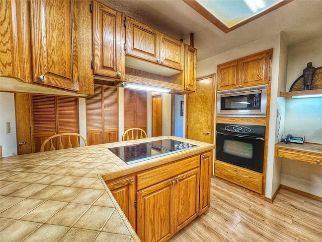 kitchen featuring light wood-type flooring, brown cabinetry, tile counters, and black appliances