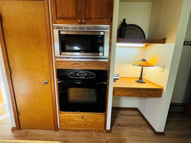 kitchen with wood finished floors, stainless steel microwave, black oven, baseboards, and brown cabinetry