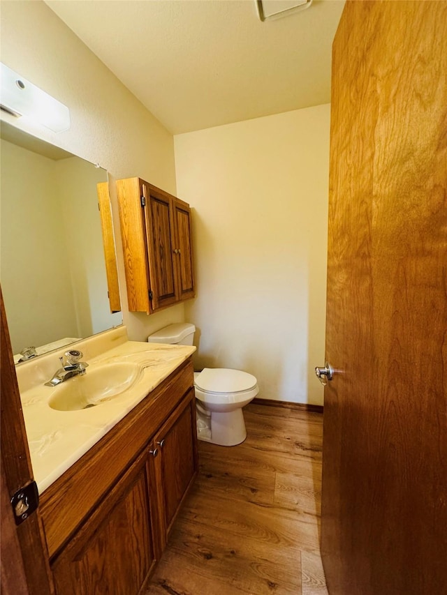 half bathroom with toilet, vanity, and wood finished floors