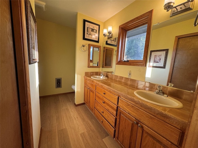 full bath featuring double vanity, wood finished floors, toilet, and a sink
