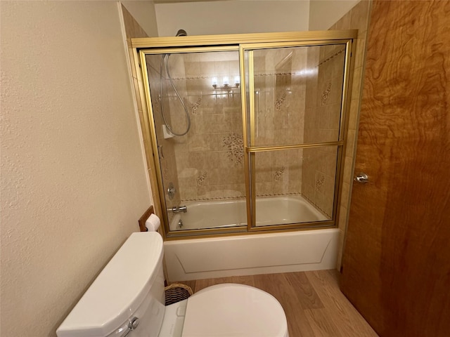 bathroom with wood finished floors, combined bath / shower with glass door, toilet, and a textured wall