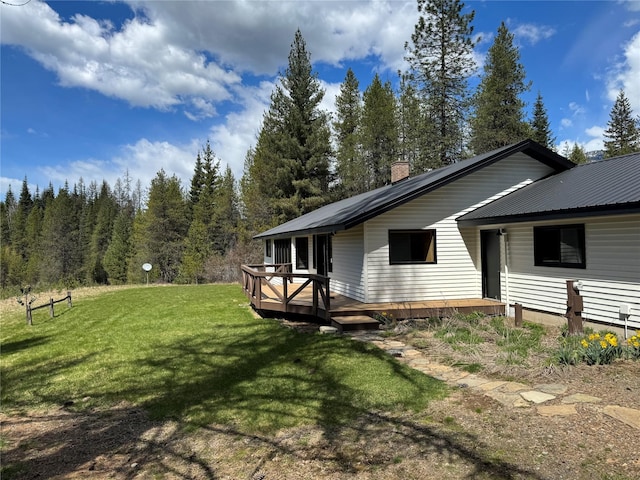 exterior space featuring a yard, a chimney, a deck, and metal roof
