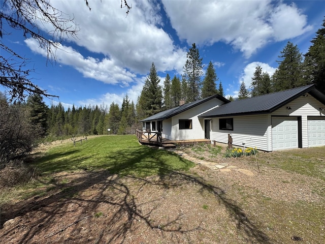 view of property exterior with metal roof, a yard, an attached garage, a view of trees, and a deck