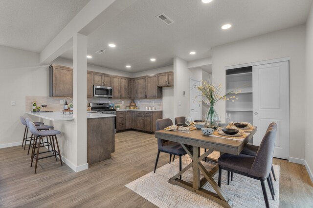 kitchen featuring decorative backsplash, stainless steel appliances, light hardwood / wood-style floors, and kitchen peninsula