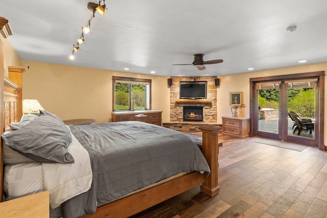 bedroom featuring wood-type flooring, ceiling fan, access to outside, and a stone fireplace