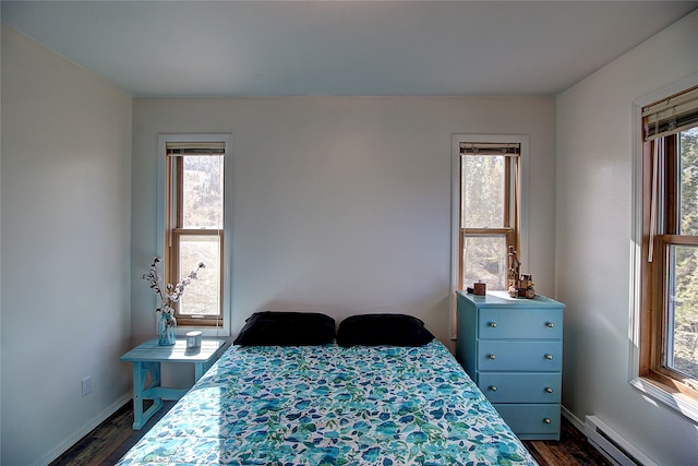 bedroom with multiple windows, dark hardwood / wood-style flooring, and a baseboard heating unit