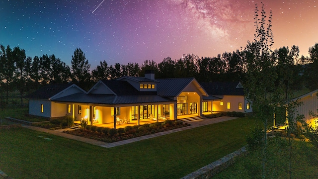 back house at dusk featuring a yard and covered porch