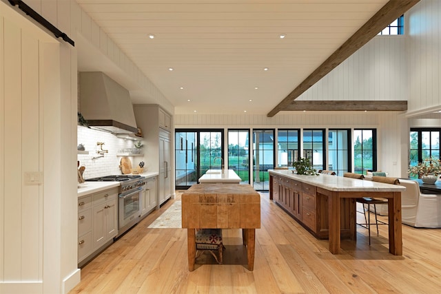 kitchen with light hardwood / wood-style flooring, gray cabinetry, stainless steel stove, and wall chimney range hood