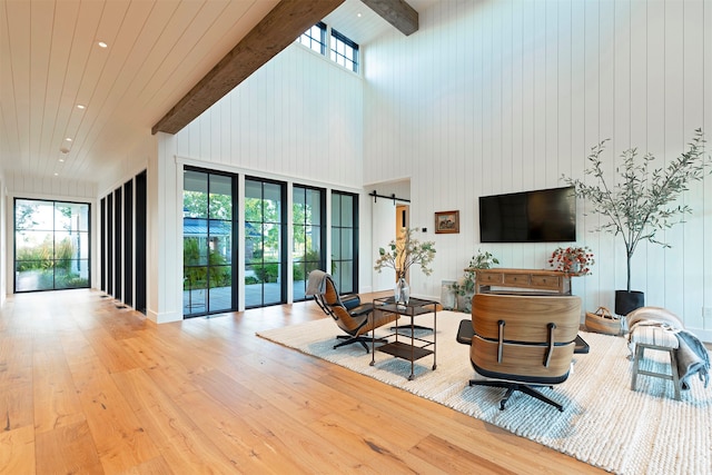 living room with a towering ceiling, beamed ceiling, a barn door, and light hardwood / wood-style floors