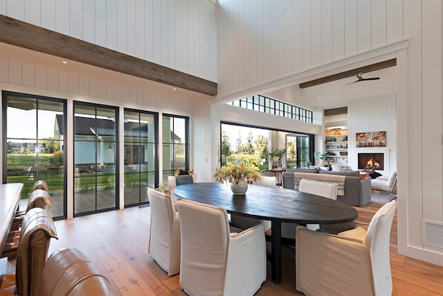 dining space with light wood-type flooring, a healthy amount of sunlight, built in shelves, and wood walls