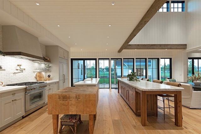 kitchen featuring high end stove, wall chimney exhaust hood, a kitchen island, and light hardwood / wood-style flooring