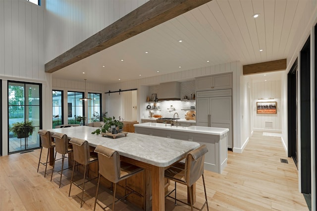 kitchen featuring gray cabinets, light hardwood / wood-style floors, a large island with sink, a barn door, and backsplash