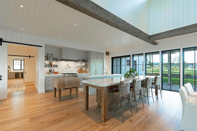 kitchen with light hardwood / wood-style flooring, beamed ceiling, tasteful backsplash, and a barn door