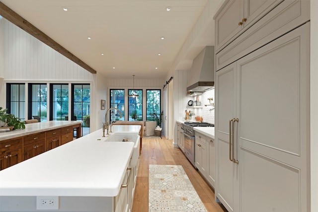 kitchen with high end stainless steel range, light hardwood / wood-style flooring, a kitchen island with sink, sink, and wall chimney range hood