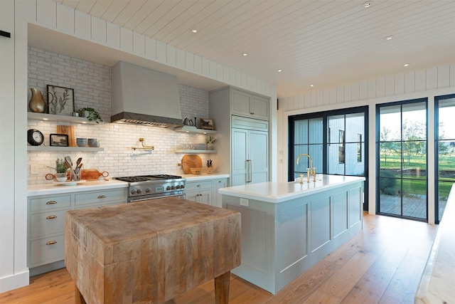 kitchen with a center island with sink, high end appliances, premium range hood, and light hardwood / wood-style flooring