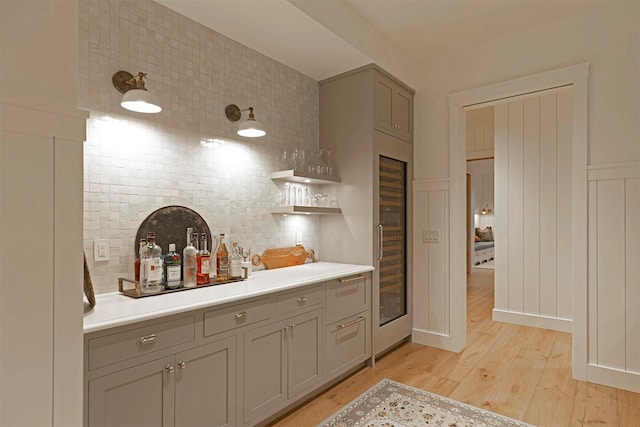 bar with gray cabinets, light wood-type flooring, beverage cooler, and tasteful backsplash