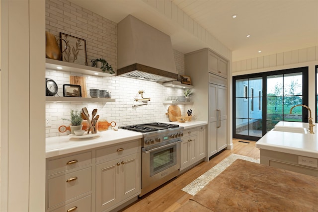 kitchen featuring stainless steel range, premium range hood, light wood-type flooring, and sink