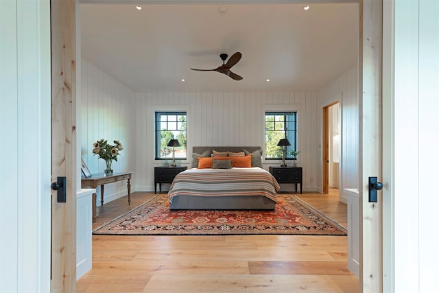 bedroom with multiple windows, wood walls, light wood-type flooring, and ceiling fan