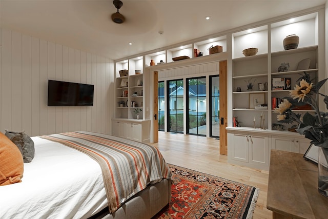 bedroom featuring ceiling fan, light hardwood / wood-style floors, wood walls, and access to exterior