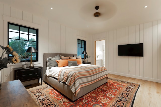 bedroom featuring light hardwood / wood-style flooring, wooden walls, ceiling fan, and ensuite bathroom