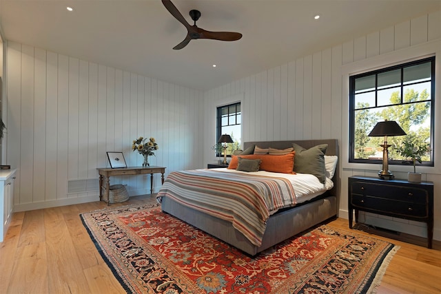 bedroom with multiple windows, wood walls, ceiling fan, and light hardwood / wood-style flooring