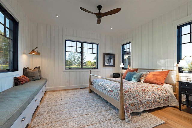 bedroom featuring ceiling fan, light wood-type flooring, and wood walls