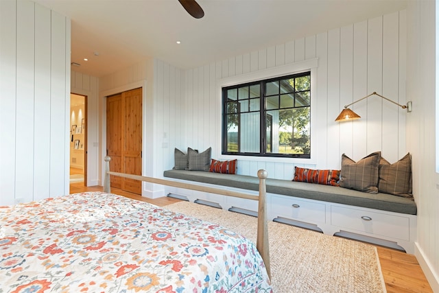 bedroom featuring ceiling fan, hardwood / wood-style flooring, a closet, and wooden walls