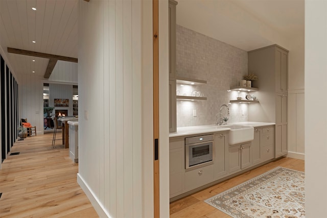 bar featuring gray cabinetry, oven, beam ceiling, light hardwood / wood-style flooring, and sink