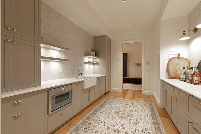 kitchen with gray cabinets, light wood-type flooring, sink, backsplash, and decorative light fixtures