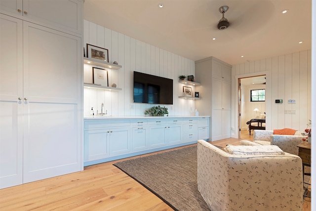 kitchen featuring white cabinetry, wood walls, light wood-type flooring, ceiling fan, and sink