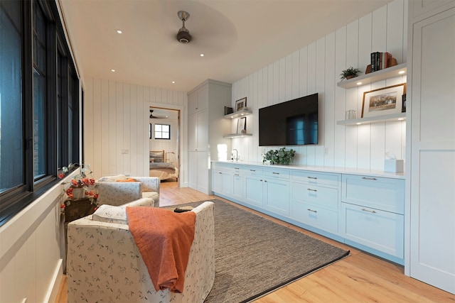 living room featuring ceiling fan, sink, wooden walls, and light hardwood / wood-style floors